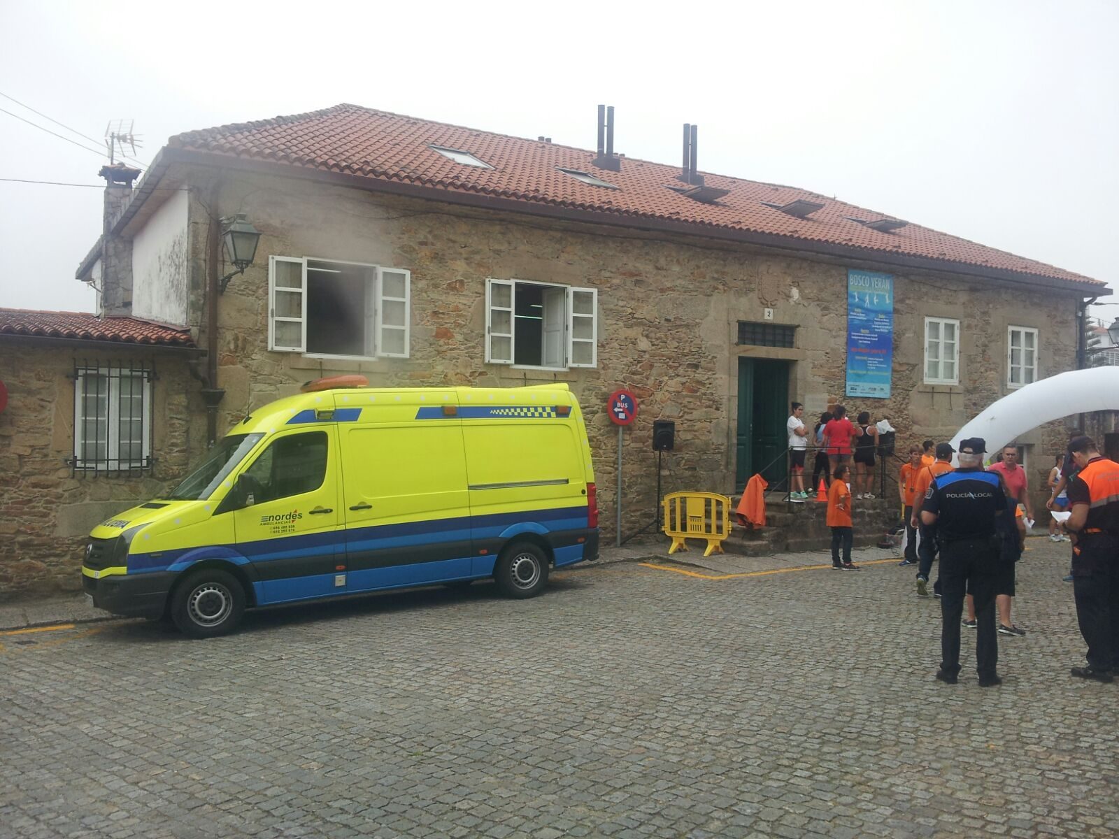Ambulancia de Ambulancias do Nordés estacionada junto a un edificio de piedra durante la cobertura de una carrera popular