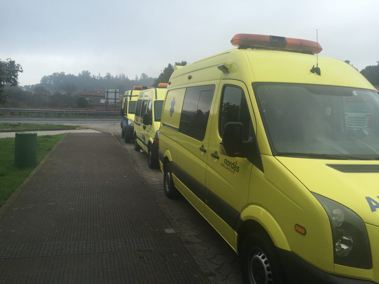 Tres ambulancias de Ambulancias do Nordés estacionadas en fila junto a la carretera en un día de niebla