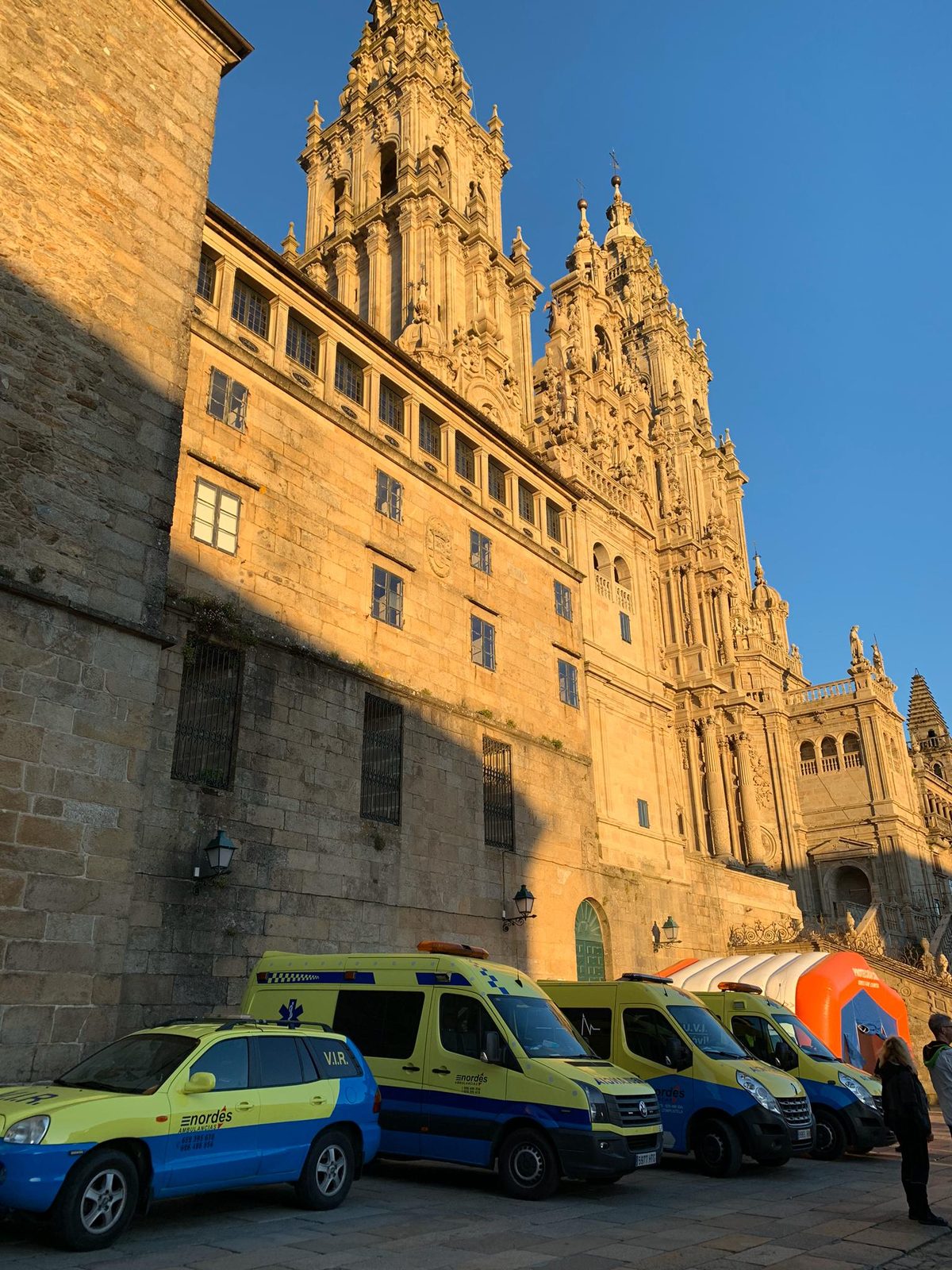 Flota de vehículos de Ambulancias do Nordés estacionada frente a la fachada del Obradoiro de la Catedral de Santiago al atardecer